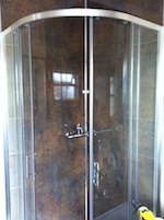 a two door curved shower cubicle with a dark marble wall