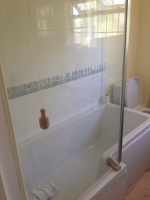 bathtub with a glass wall and slight L shaped wider shower area