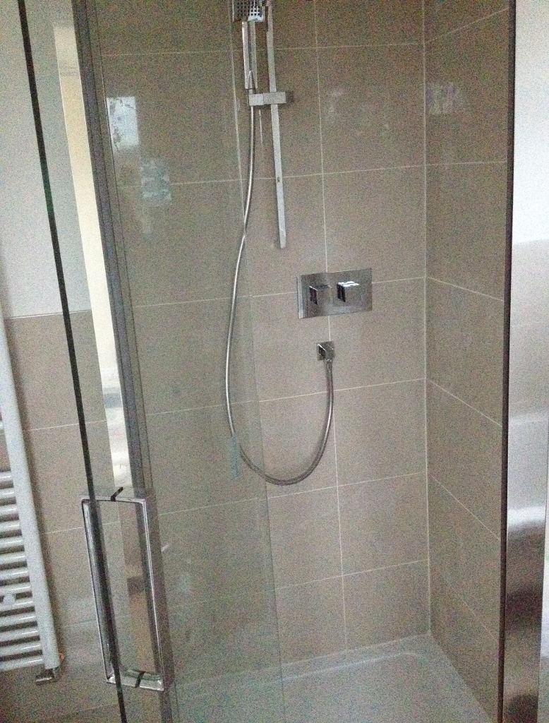square shower cubicle with tan tiles and square chrome controls